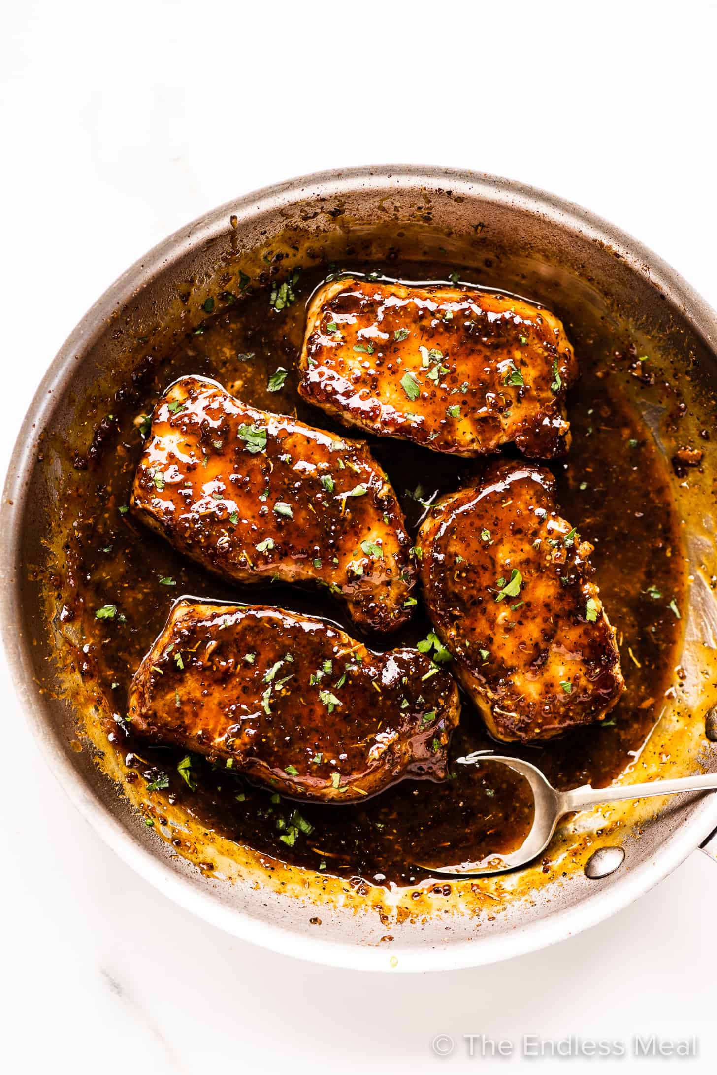 a spoon pouring honey mustard sauce over pork chops in a pan
