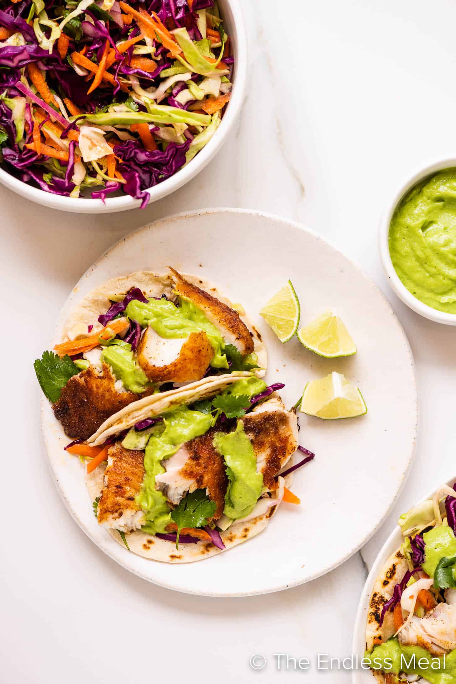Baja Fish Tacos on a plate with avocado sauce and slaw on the side.