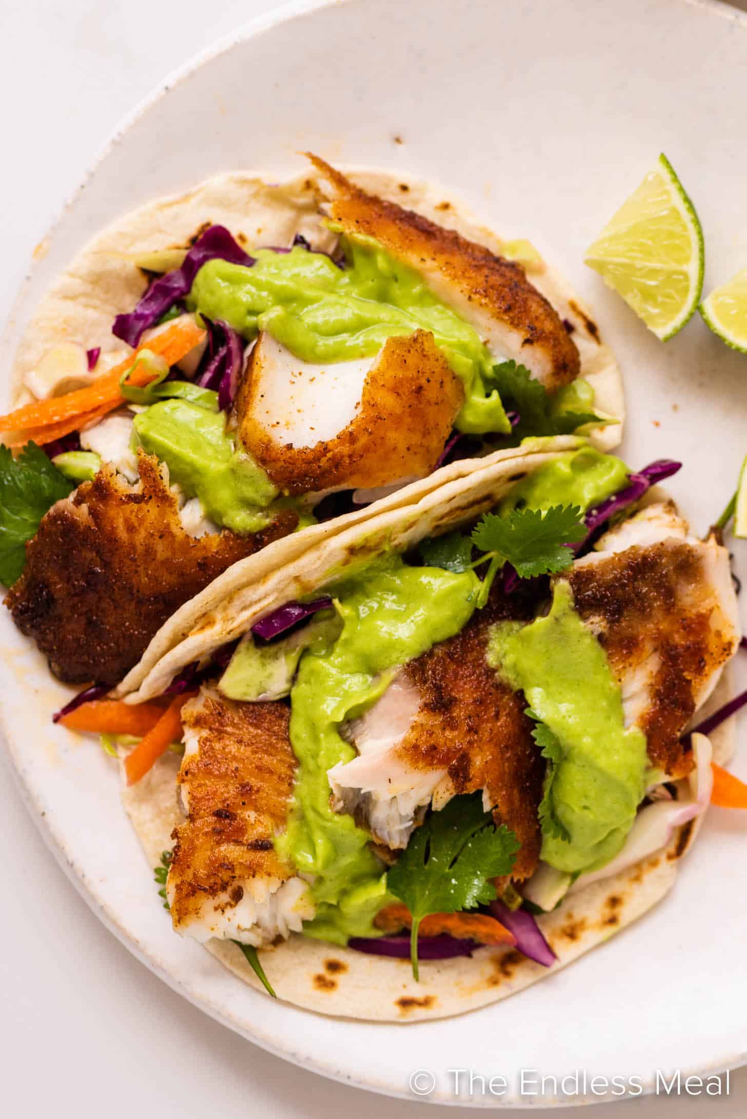 two Baja Fish Tacos on a plate with avocado sauce