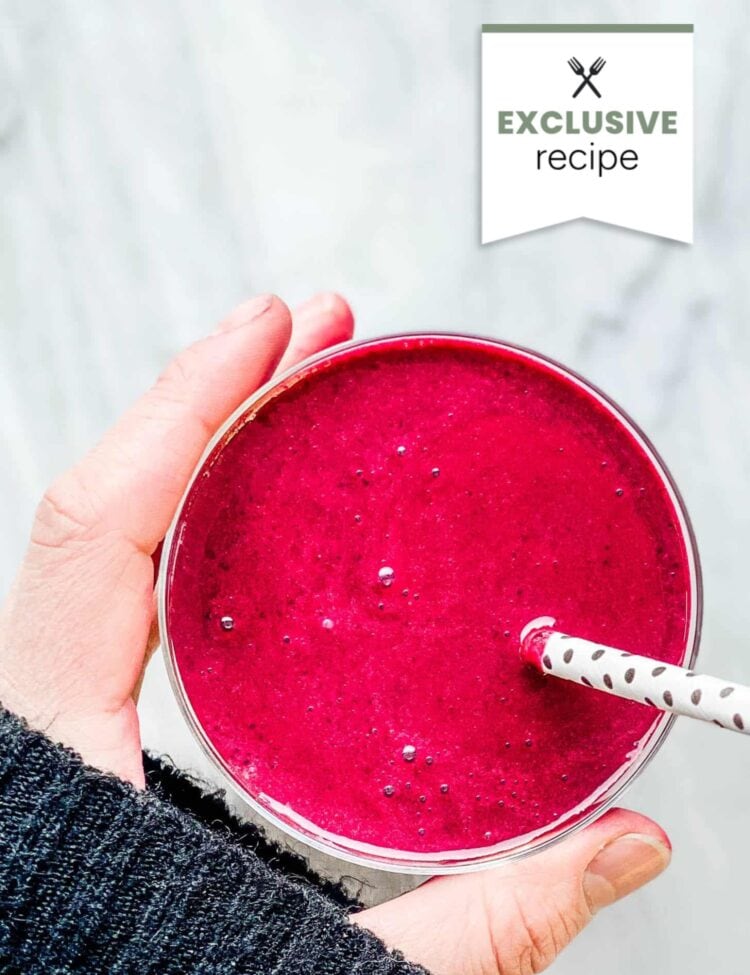 A hand holding a glass of bright pink Blackberry Lemonade smoothie with a white straw on a light surface; “EXCLUSIVE recipe” tag at the top right.
