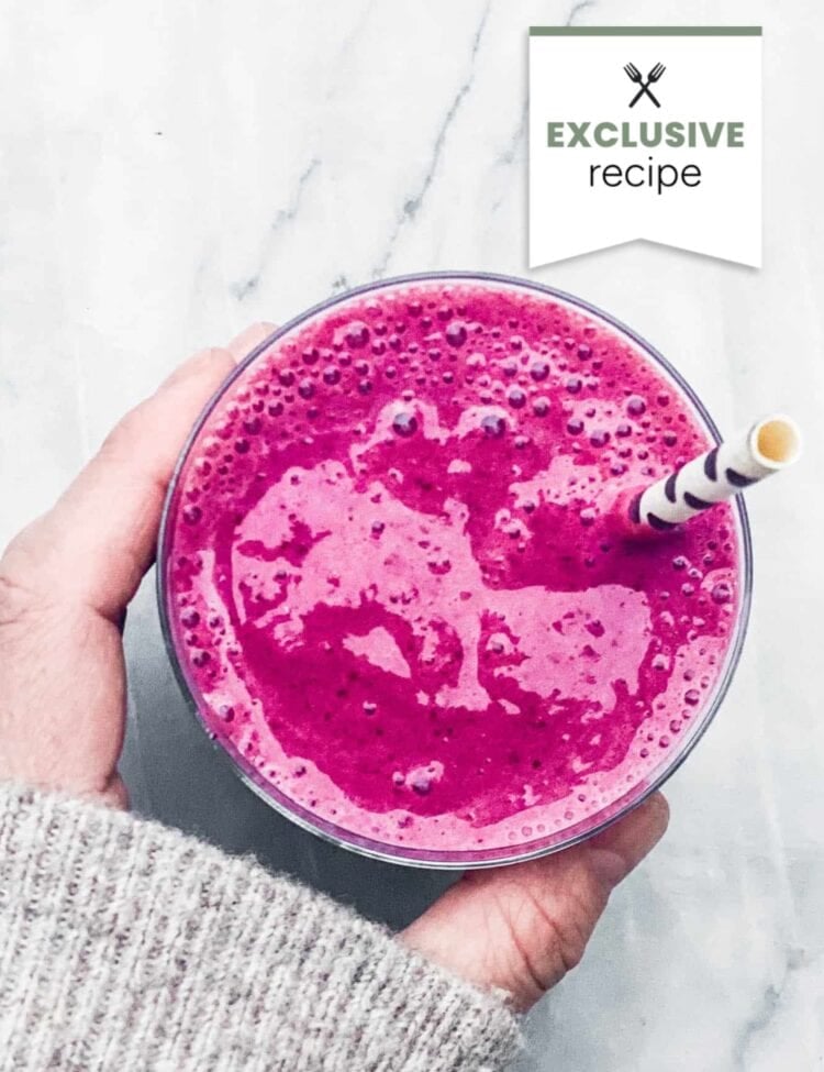A hand holding a glass of bright pink Blackberry Lemonade smoothie with a striped straw on a white surface; “Exclusive recipe” text appears at the top right.