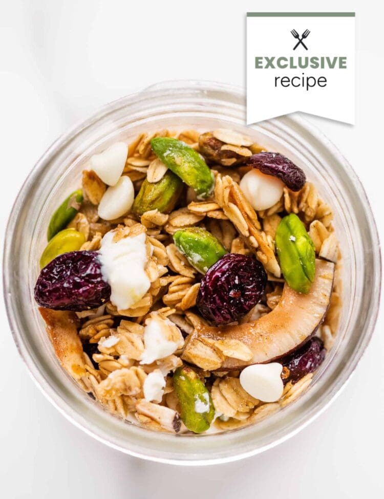A glass jar filled with granola, dried cranberries, pistachios, coconut flakes, and white chocolate chips. A hint of Blackberry Lemonade flavor brightens this exclusive recipe—perfect for a unique and refreshing snack.