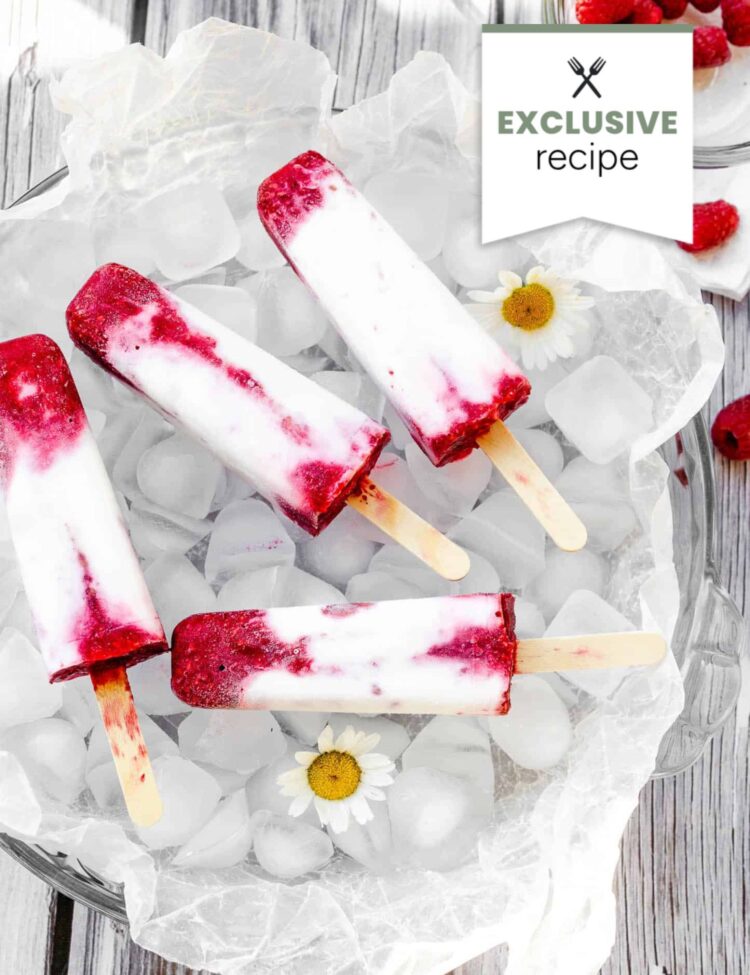 Four berry and cream popsicles are arranged on ice in a clear bowl, with fresh raspberries, daisies, and a hint of Blackberry Lemonade nearby. A tag reads EXCLUSIVE recipe.