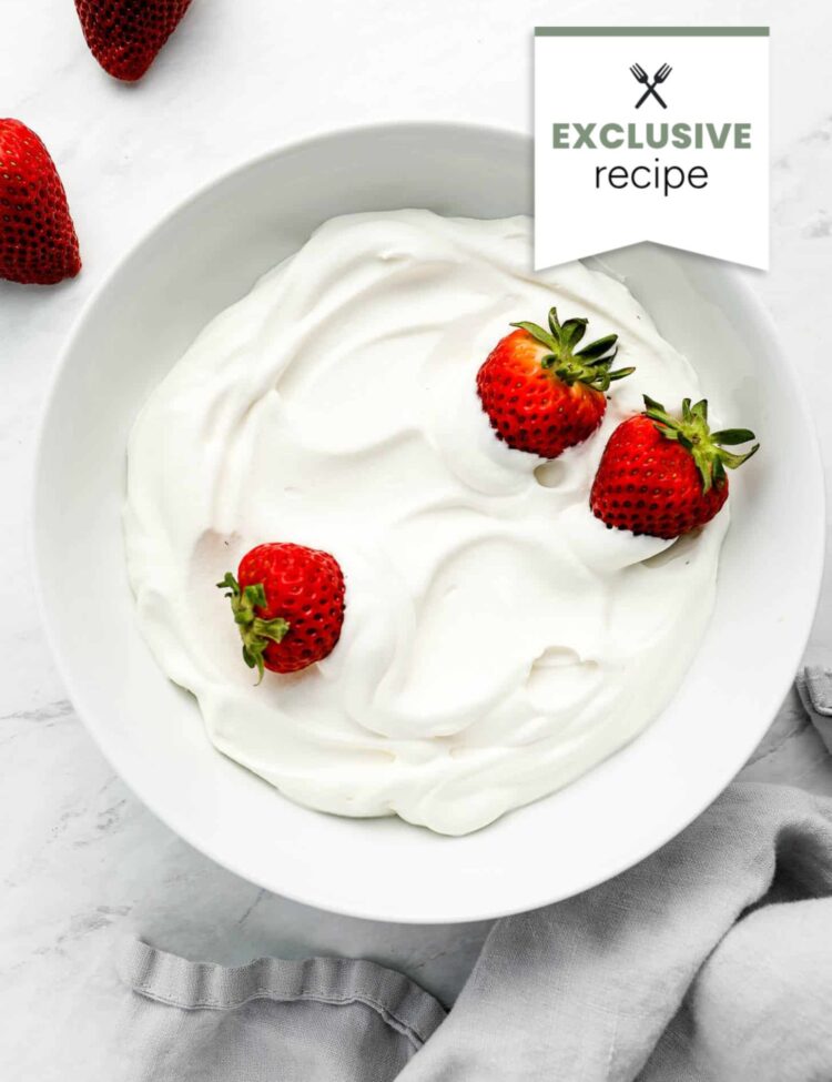 A white bowl filled with whipped cream and topped with three strawberries, perfect alongside a refreshing glass of Blackberry Lemonade.