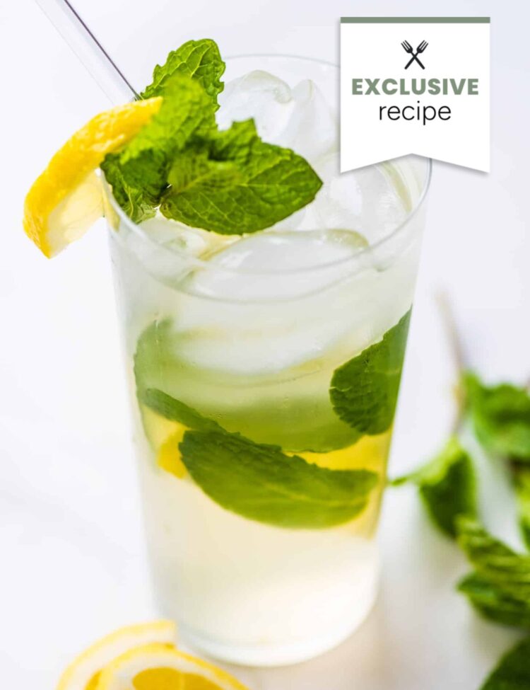 A glass of refreshing blackberry lemonade garnished with fresh mint leaves and a lemon slice, with a straw and extra lemon slices nearby.