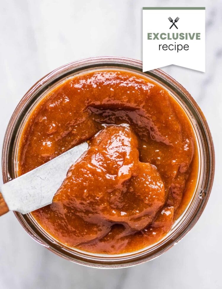 A jar of thick, reddish-brown sauce with a knife inside, viewed from above. A label in the corner reads EXCLUSIVE Blackberry Lemonade recipe.