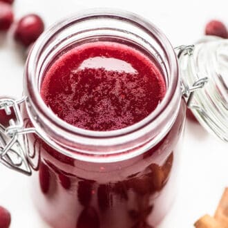 Cranberry Simple Syrup in a glass jar surrounded by spices