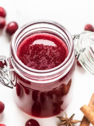 Cranberry Simple Syrup in a glass jar surrounded by spices
