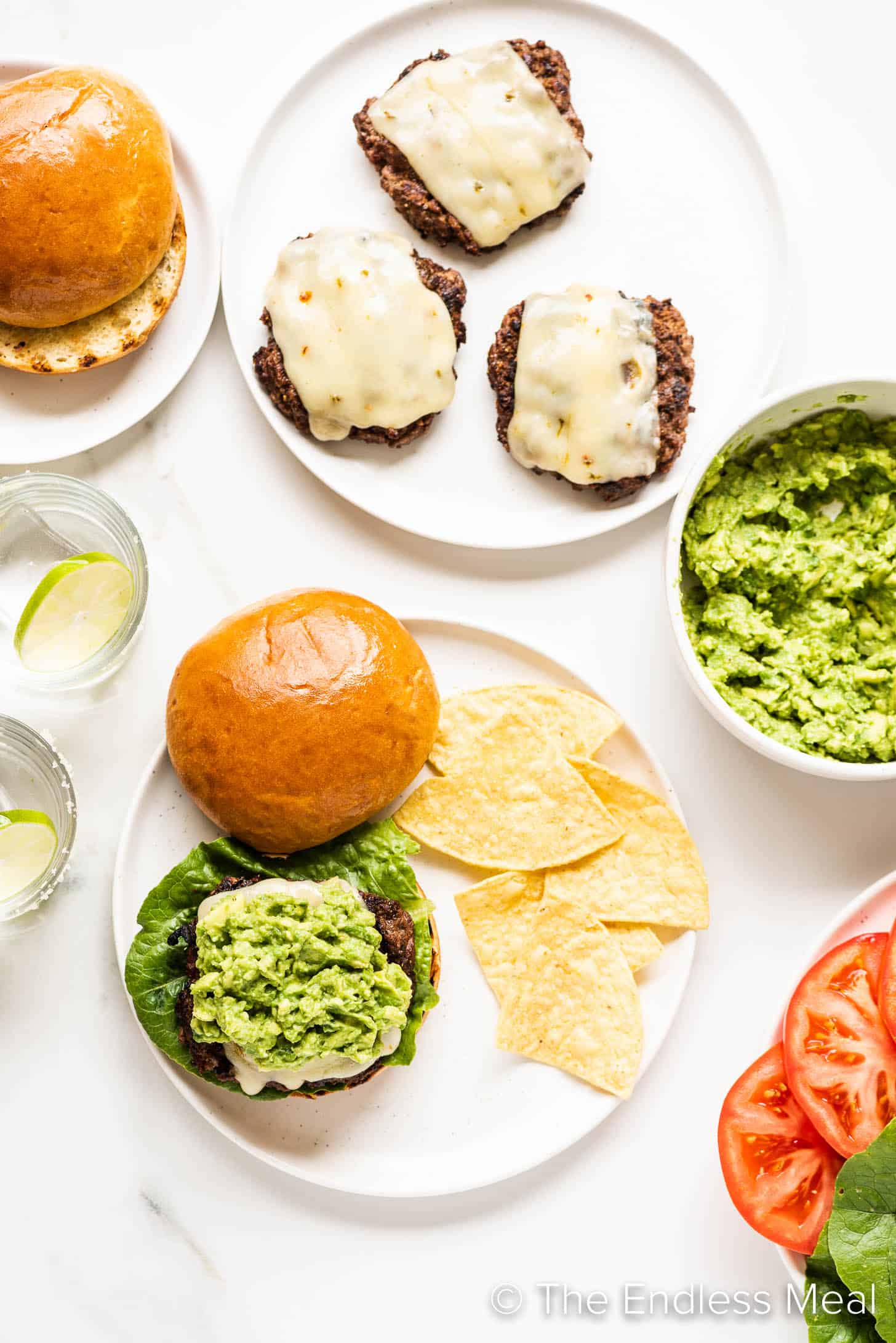 a guacamole topped burger on a table with all the fixings around.