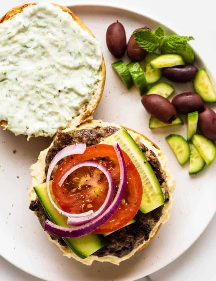 a lamb burger with hummus and tzatziki on a plate