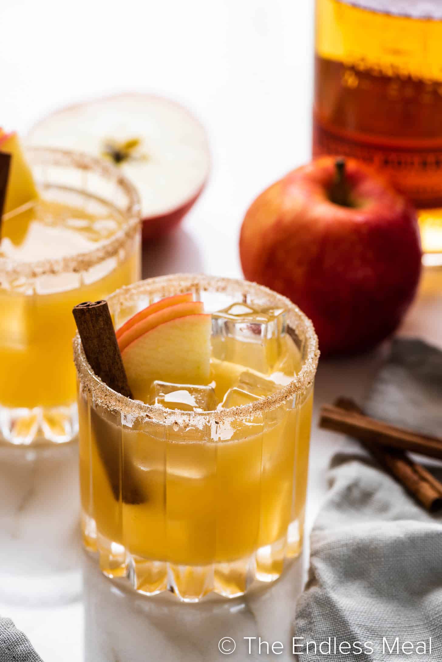two glasses of Apple Bourbon Smash in front of a bourbon bottle