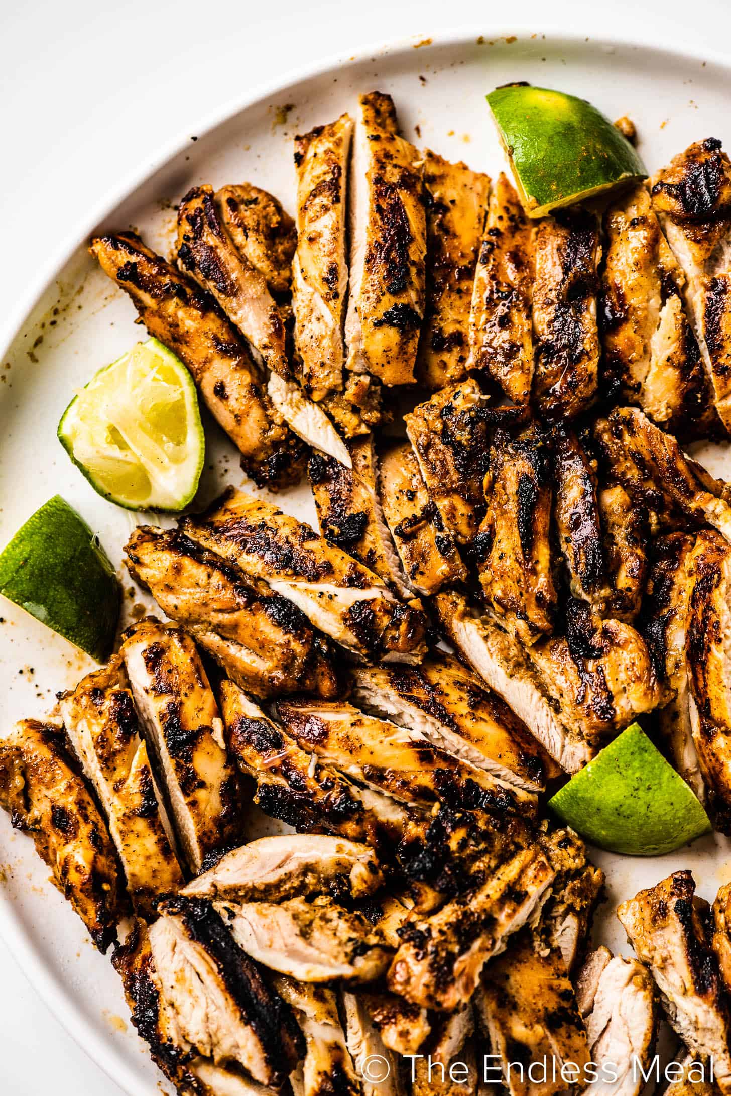 chicken cooked in Jerk Chicken Marinade sliced on a plate with limes. 