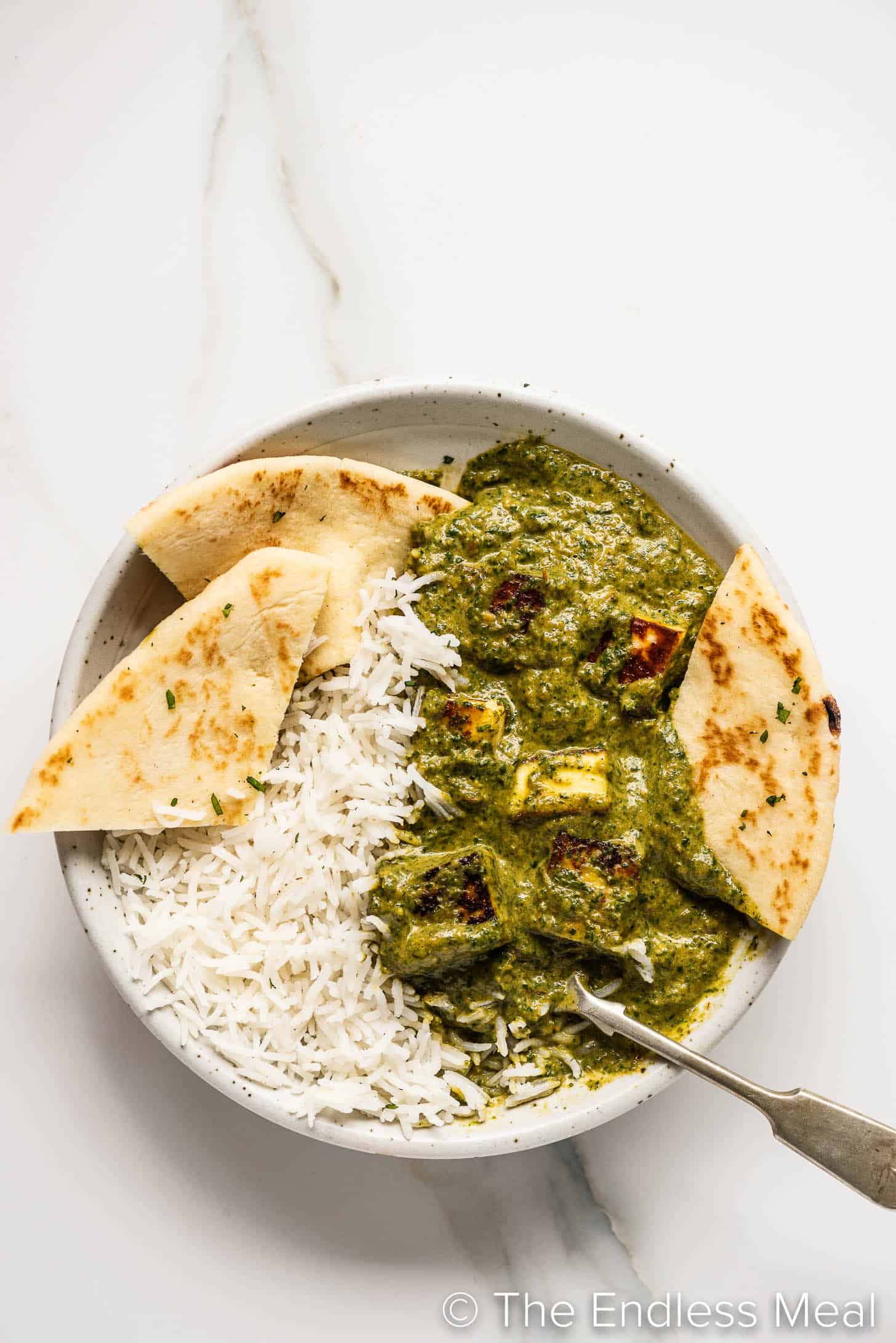 spinach curry with paneer in a bowl with rice and naan