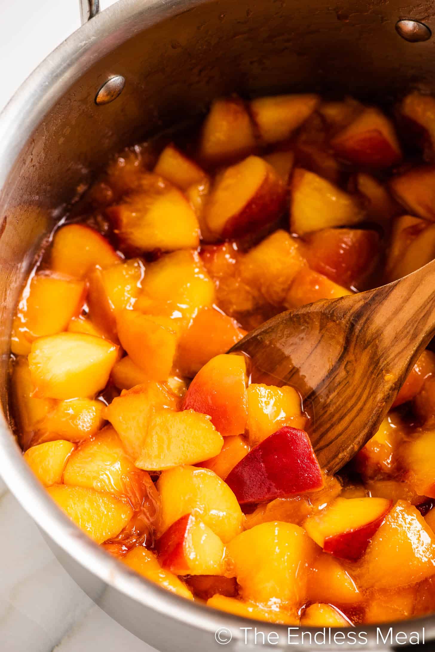a wooden spoon stirring a pot of Peach Compote