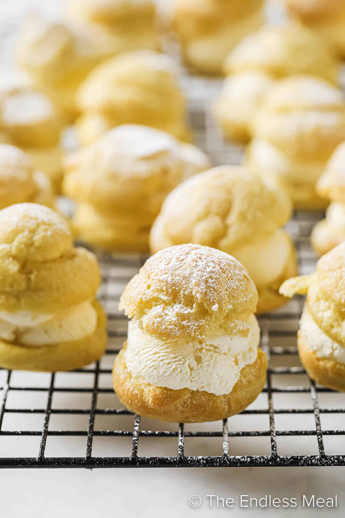 profiteroles filled with whipped cream on a cooling rack.