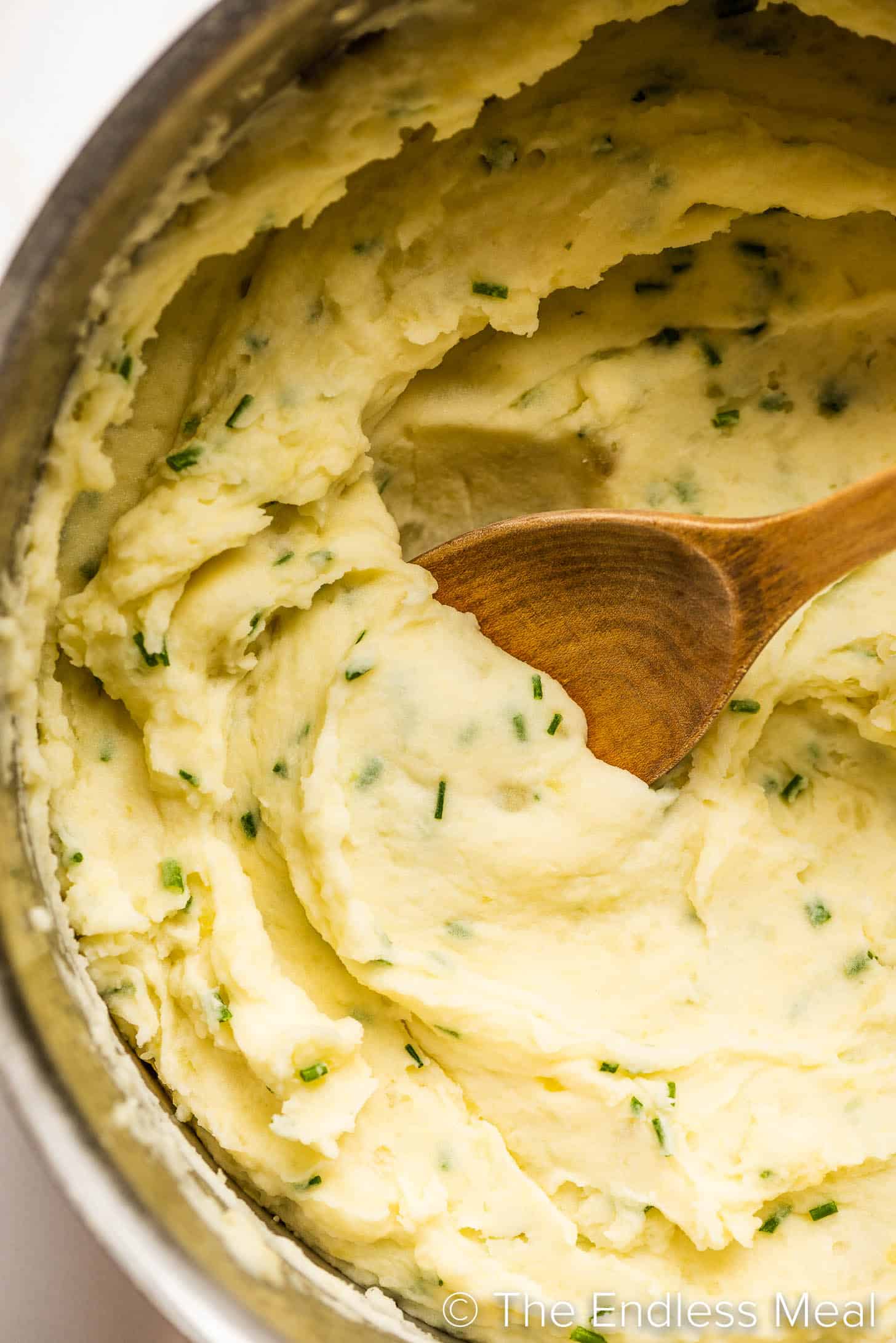Sour Cream and Chive Mashed Potatoes in a pot with a wooden spoon