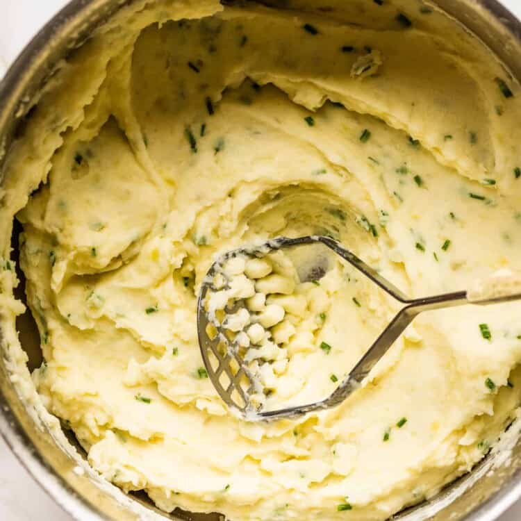 Sour Cream and Chive Mashed Potatoes in a pot with a potato masher