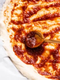 a spoon spreading Sweet Spicy Pizza Sauce on a pizza crust