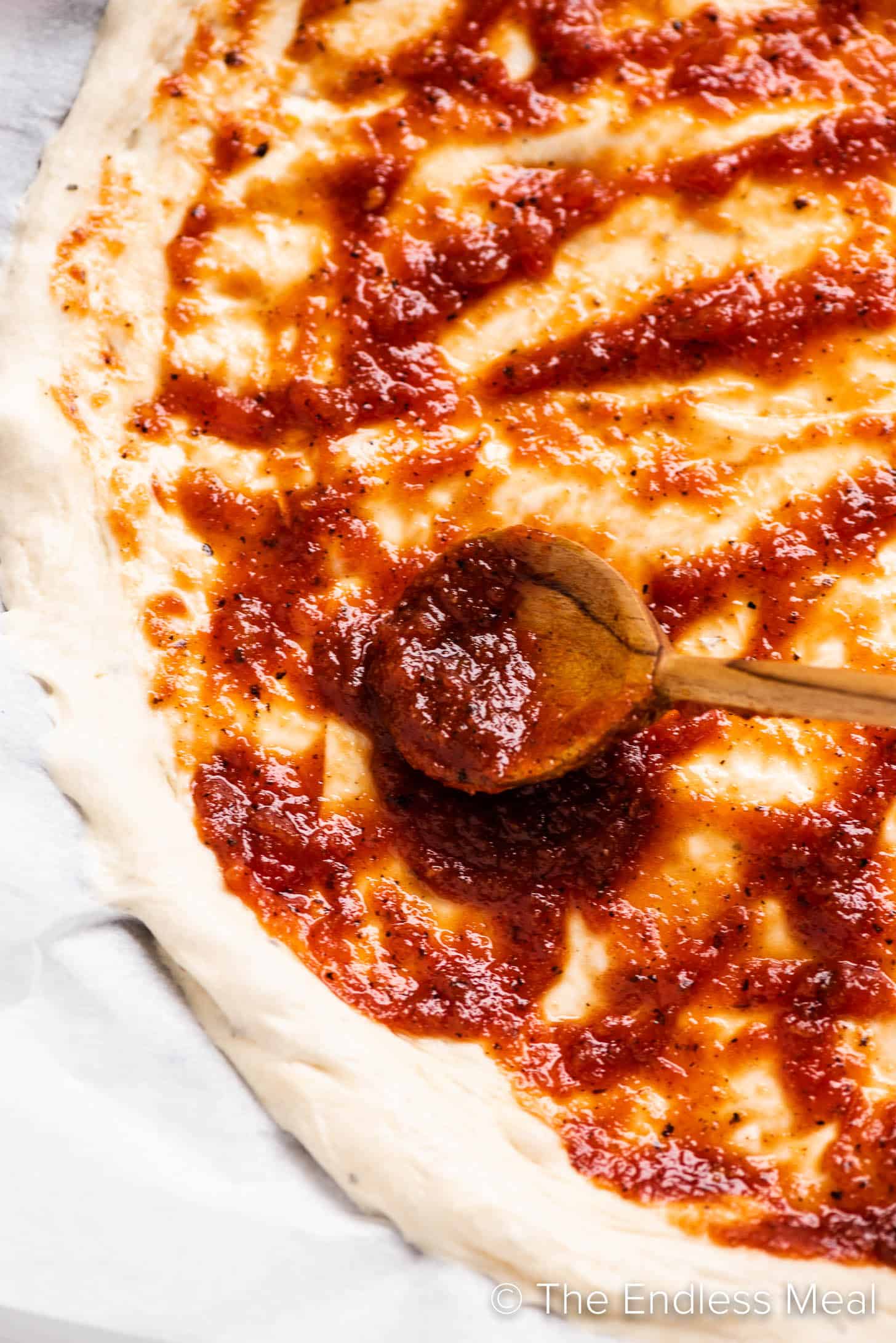 a spoon spreading Sweet Spicy Pizza Sauce on a pizza crust