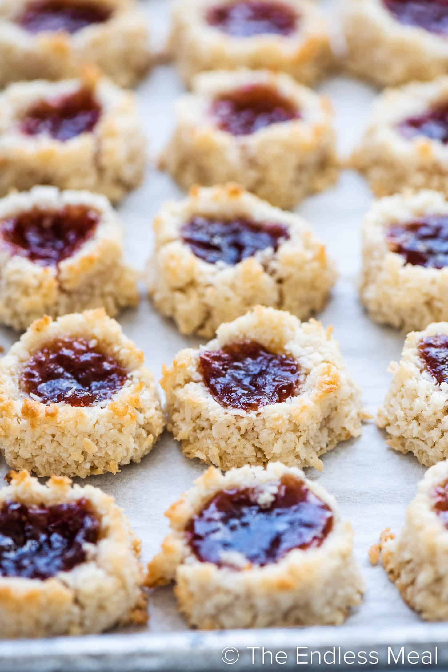 A close up of jam-filled coconut thumbprint macaroons on a baking sheet.