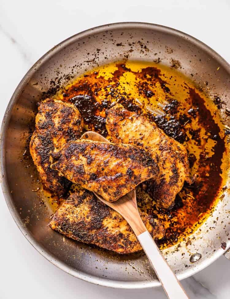 Italian Seasoning Chicken Breasts in a pan with a wooden spoon