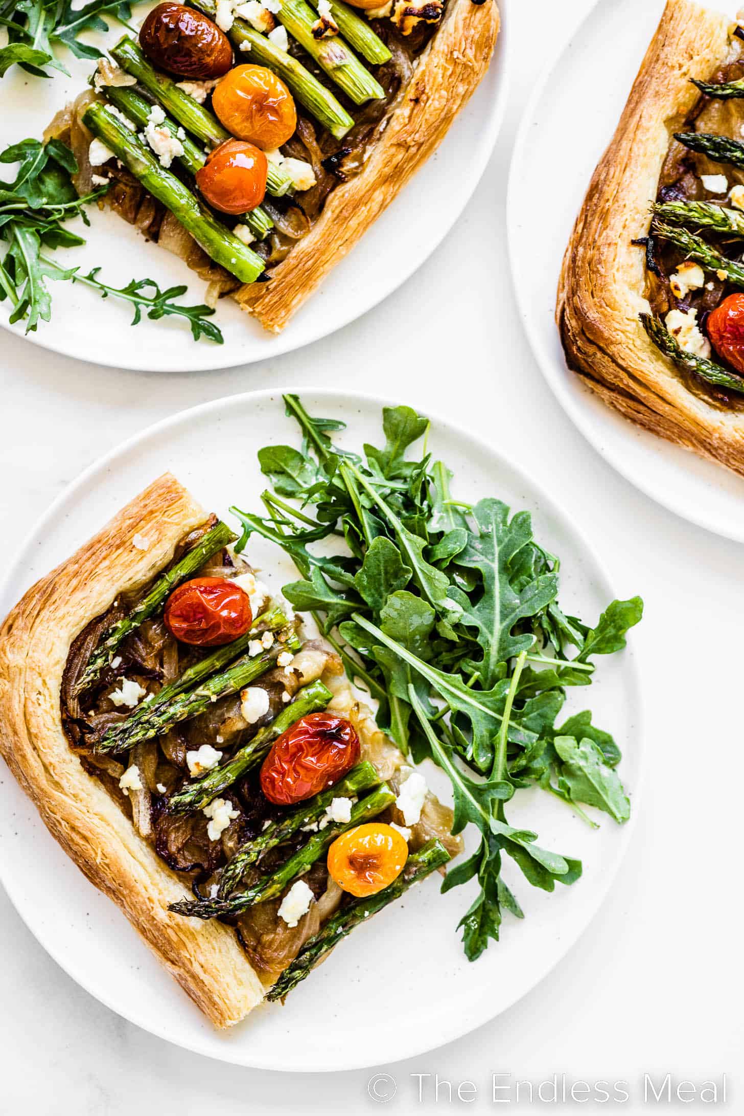 a slice of puff pastry tart with asparagus on a plate with a salad.