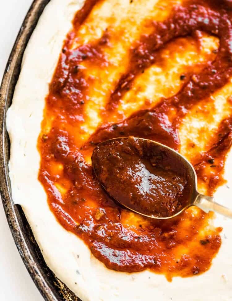 homemade pizza sauce being spread on a pizza crust