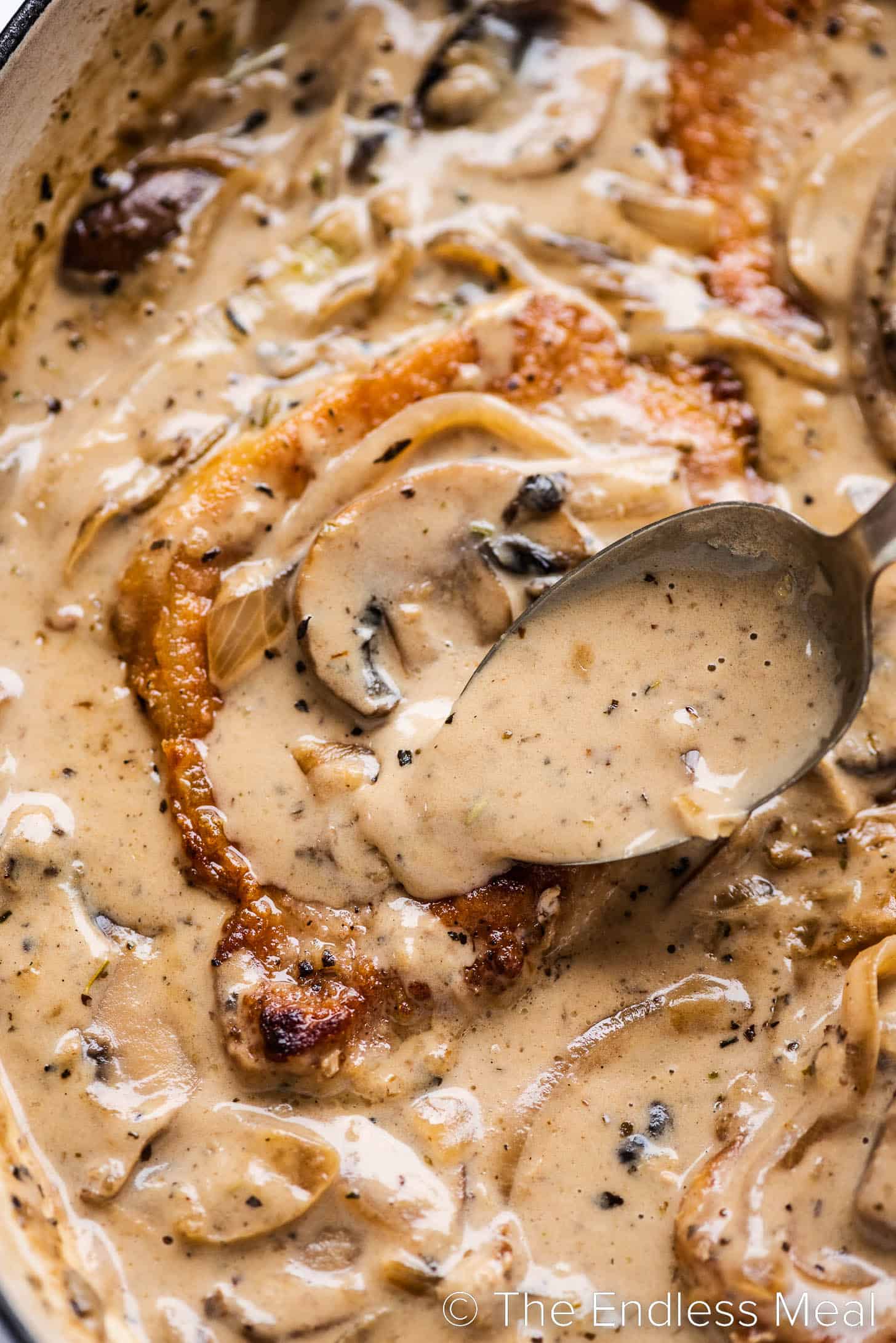 a close up of mushroom onion gravy being spooned over pork chops