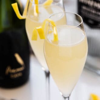 Two French 75 champagne cocktails beside a bottle of sparkling wine.