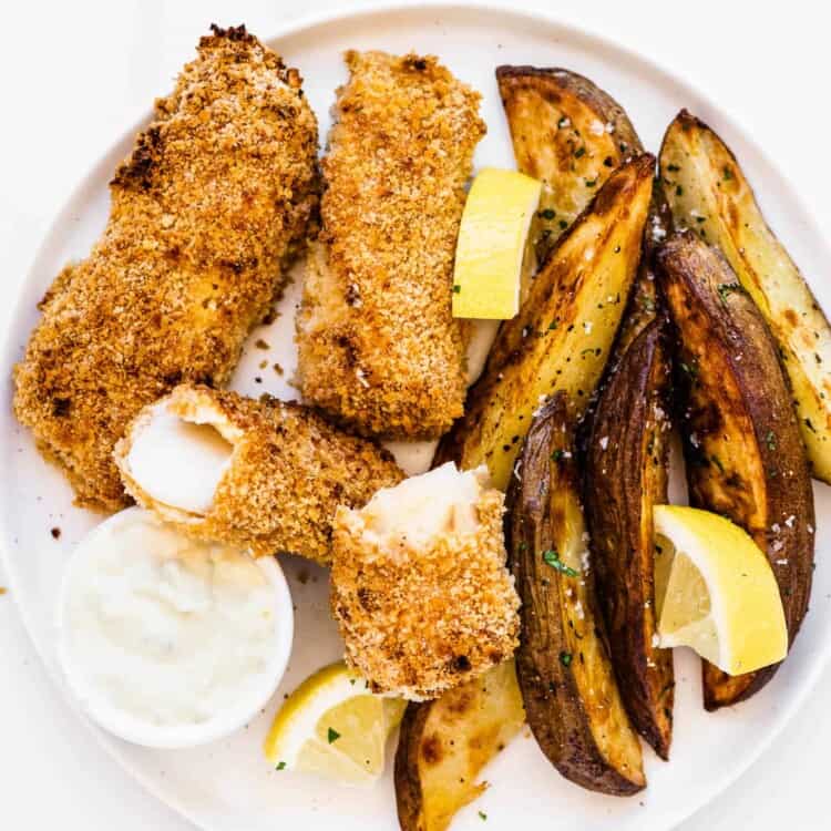 a plate of Baked Fish and Chips with tartar sauce and lemon wedges