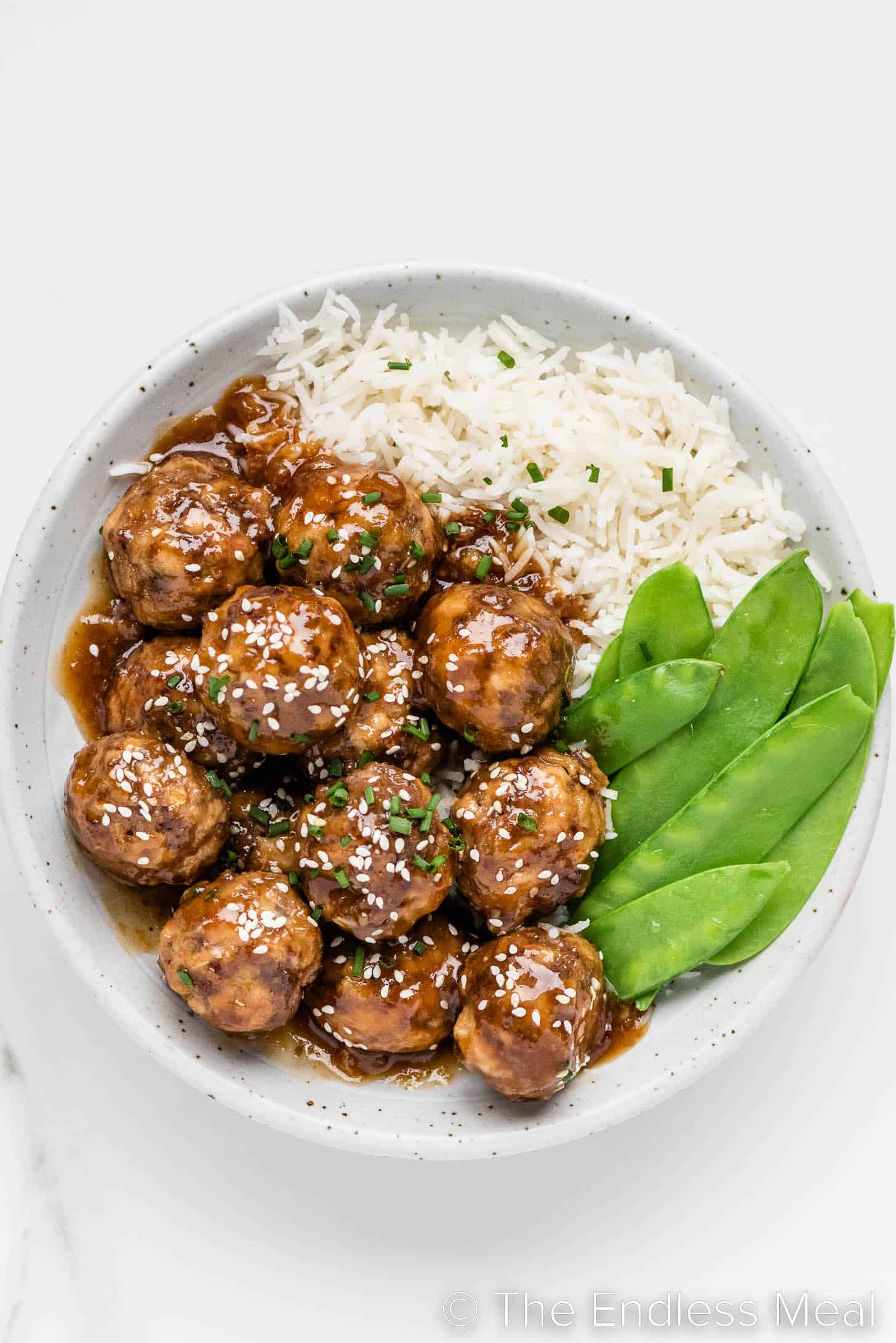 Honey Garlic Meatballs on a plate with rice and snow peas.