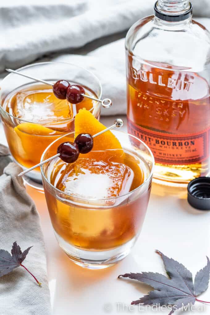 Two Maple Old Fashioned drinks with a bottle of bourbon behind them.