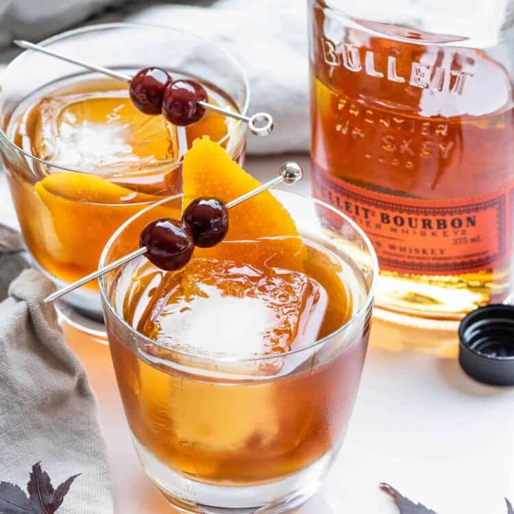 Two Maple Old Fashioned drinks with a bottle of bourbon behind them.