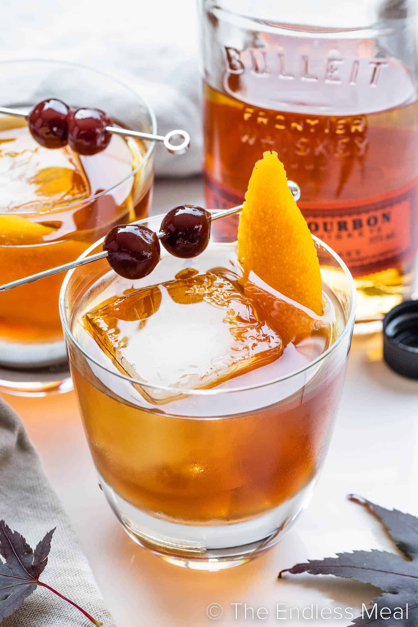 Maple Old Fashioned cocktail garnished with cherries and an orange peel 
