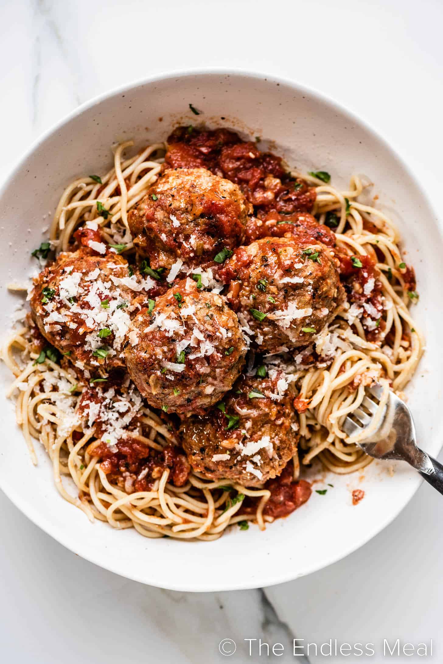 Meatballs in Tomato Sauce in a white bowl on top of spaghetti