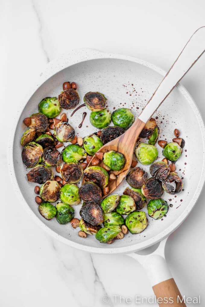 brussels sprouts being pan fried in a white frying pan