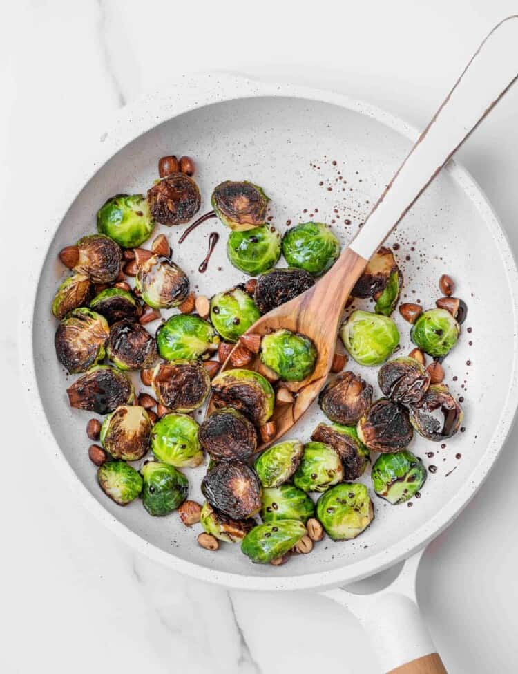 brussels sprouts being pan fried in a white frying pan