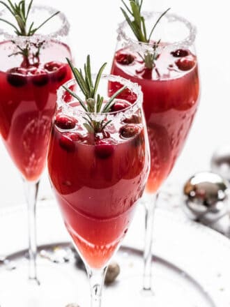 Three Christmas Mimosa garnished with cranberries and rosemary