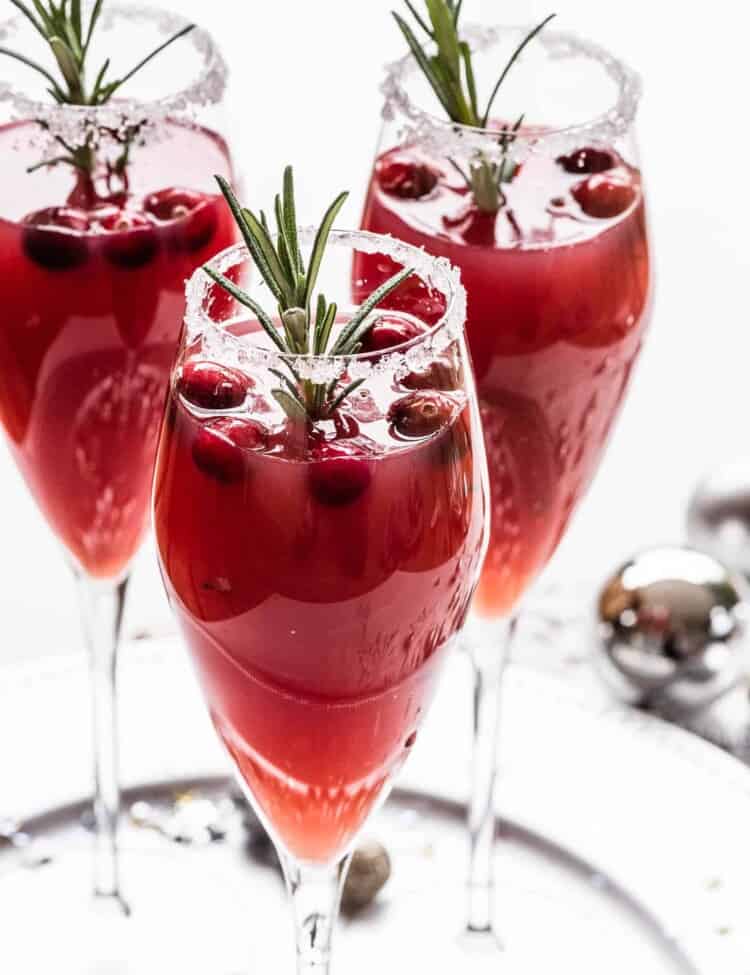 Three Christmas Mimosa garnished with cranberries and rosemary
