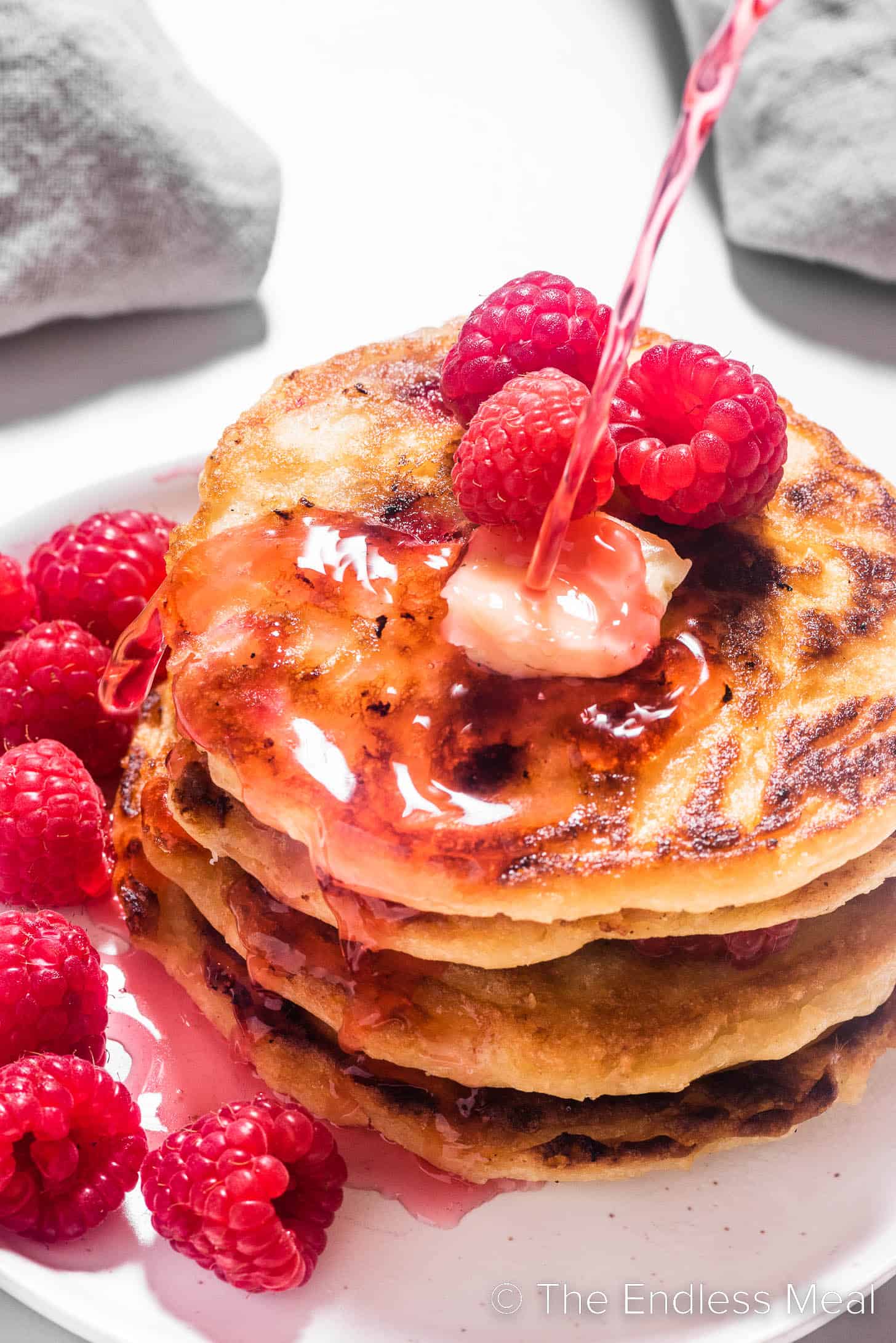 Raspberry syrup being poured over a stack of pancakes