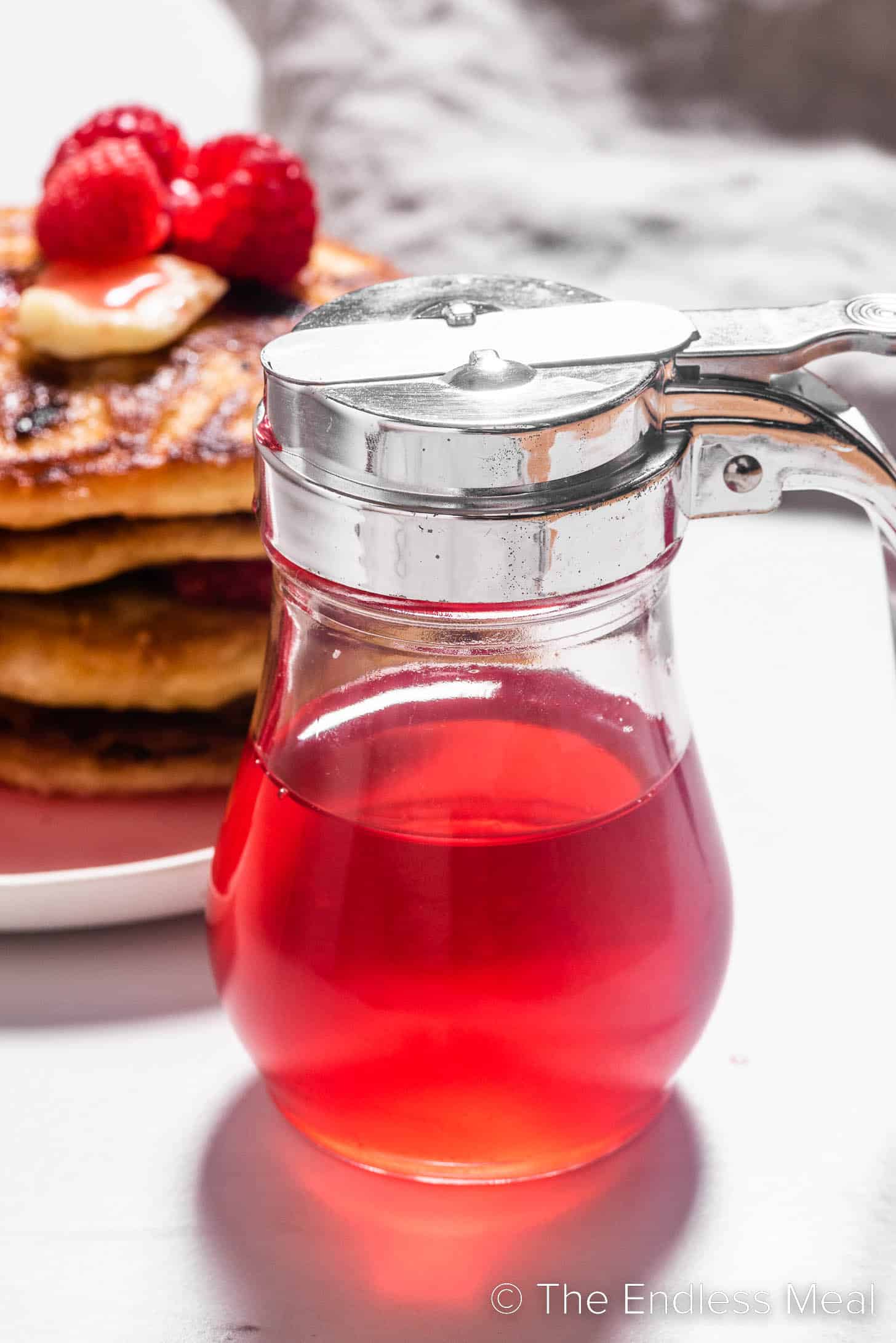 Raspberry Simple Syrup next to a stack pf pancakes