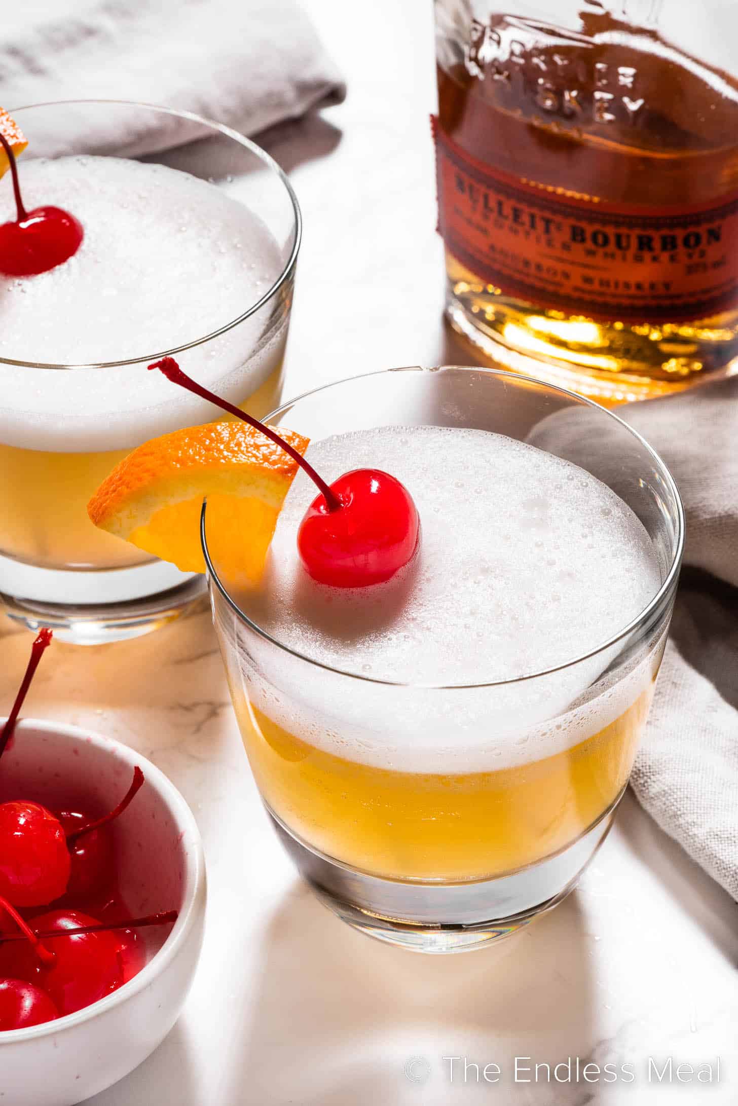 Two bourbon sour cocktails next to a bottle of bourbon