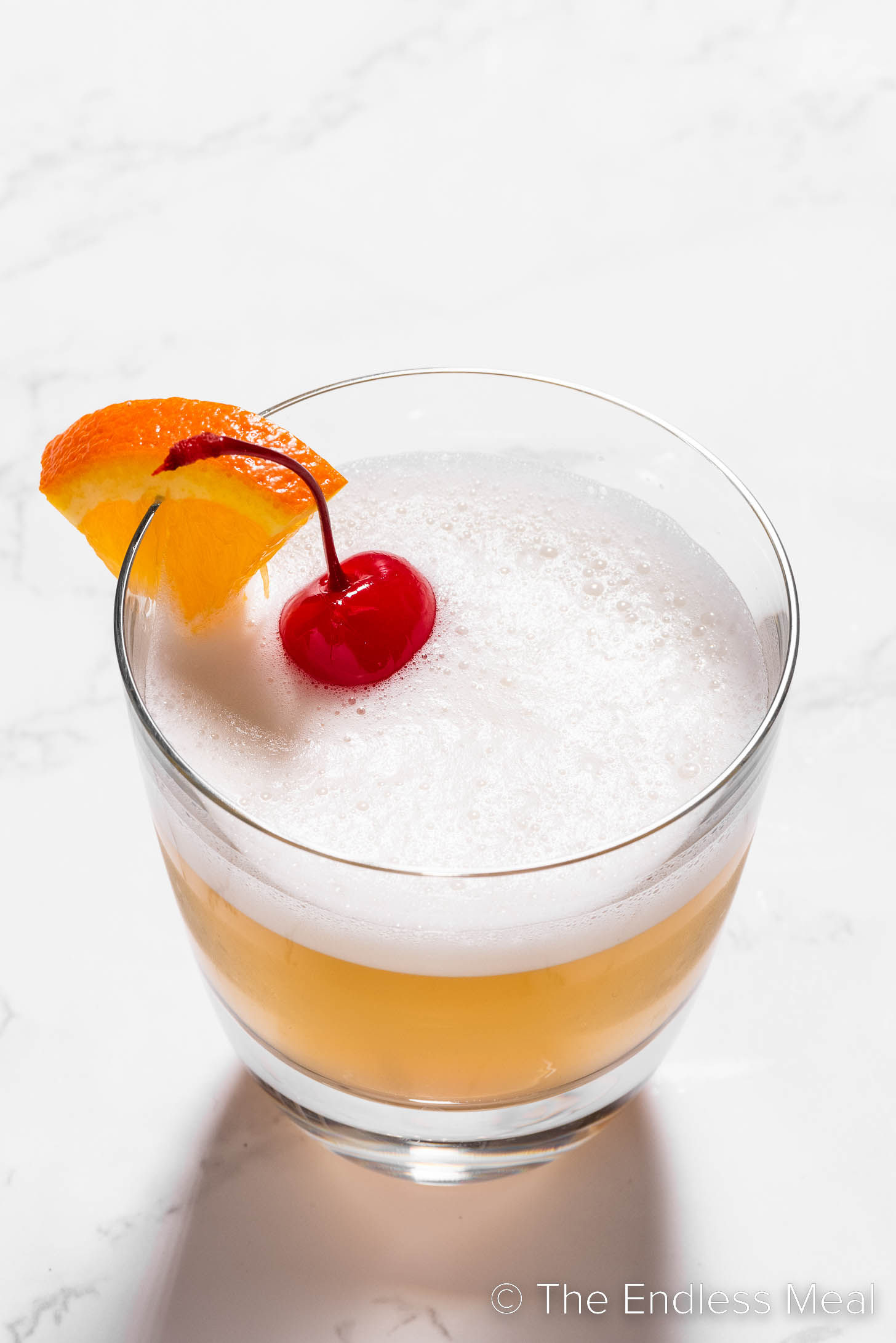 The Best Bourbon Sour garnished with a cocktail cherry and orange wedge.