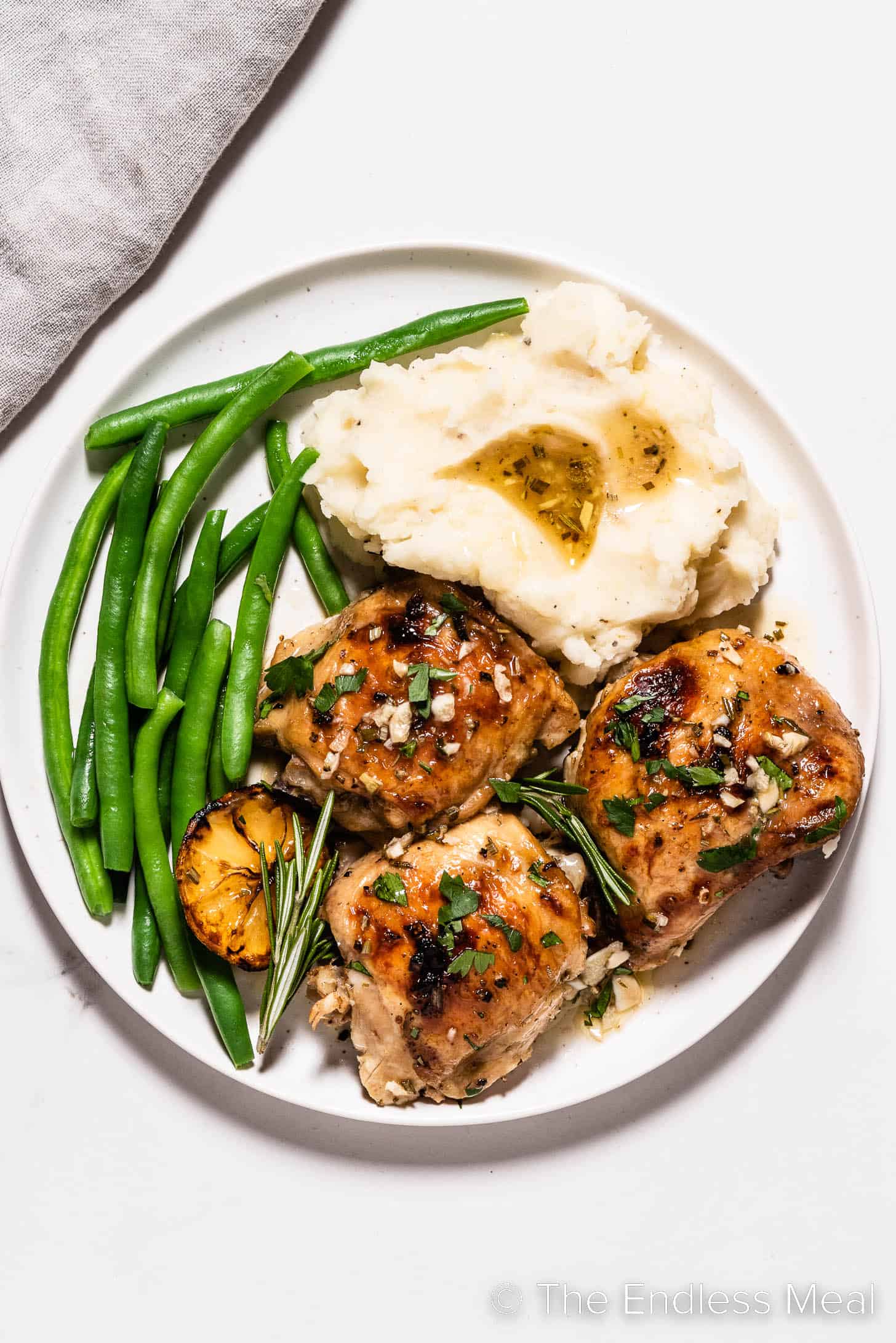 Lemon Rosemary Chicken Thighs on a plate with mashed potatoes and green beans.