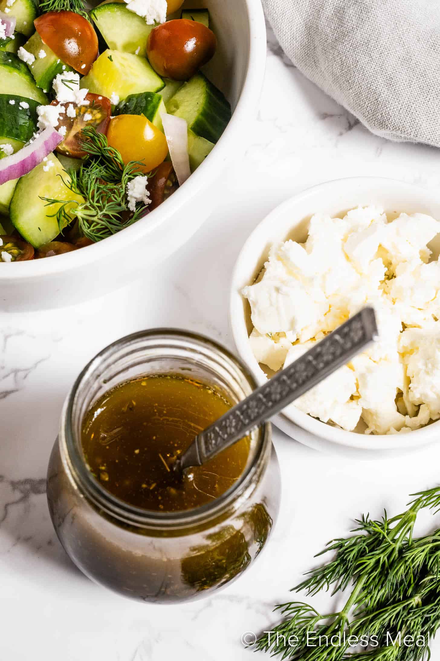 Greek Salad Dressing in a jar next to a Greek salad