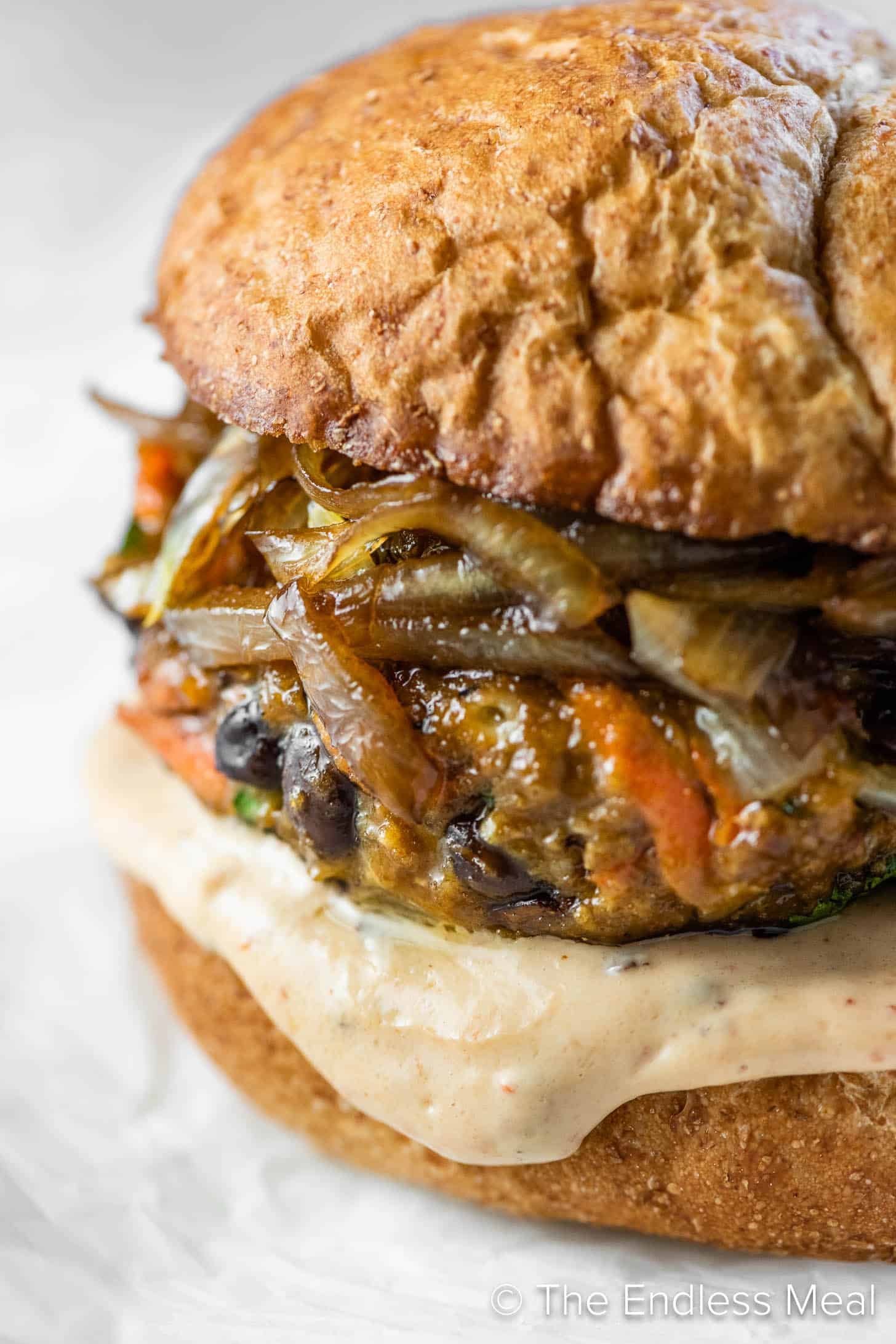 Close up of a black bean veggie burger in a bun with chipotle mayonnaise and caramelized onions