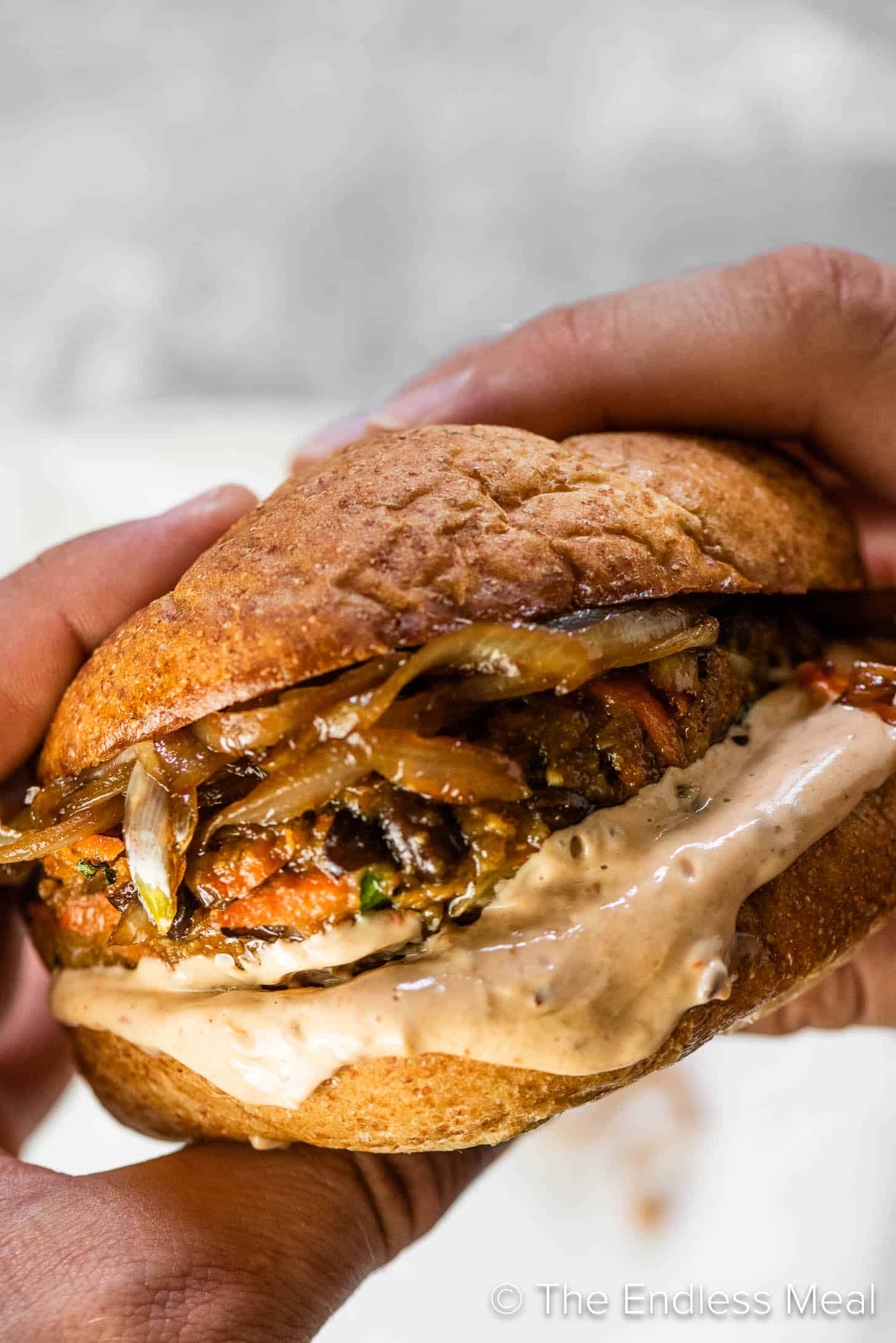 Two hands holding a black bean veggie burger with lots of chipotle mayo and caramelized onions