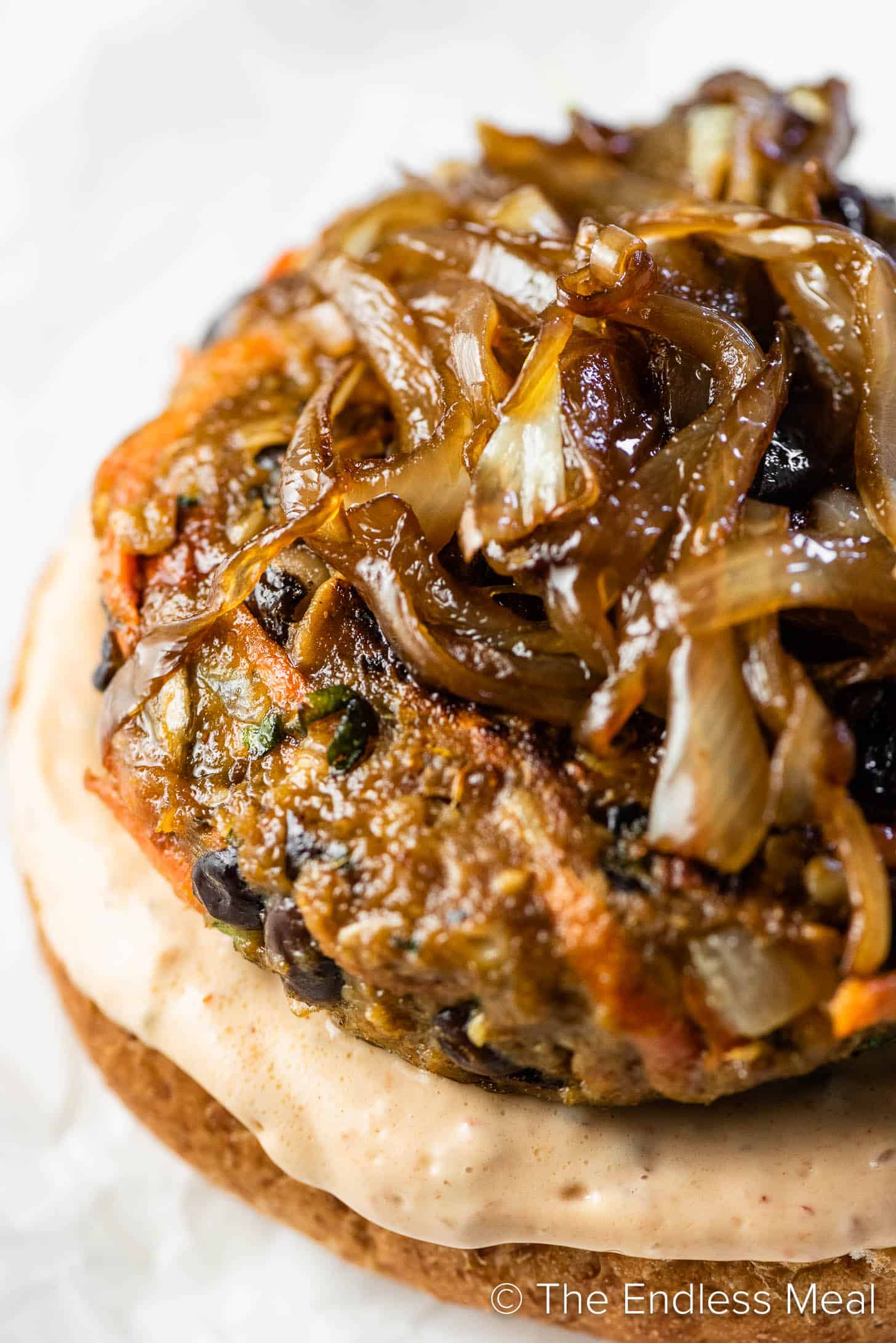 Close up of a black bean veggie burger on a white plate with caramelized onions on top