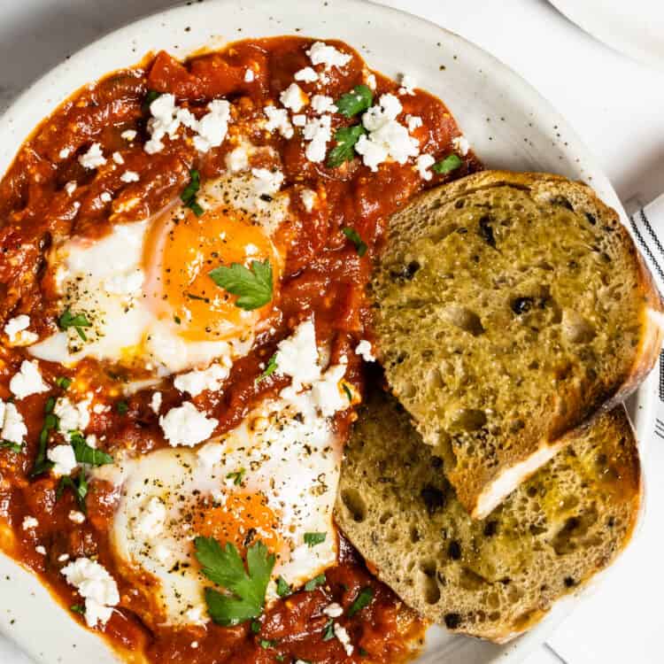 A close up of spicy shakshuka with harissa in a bowl with a slice of sourdough bread