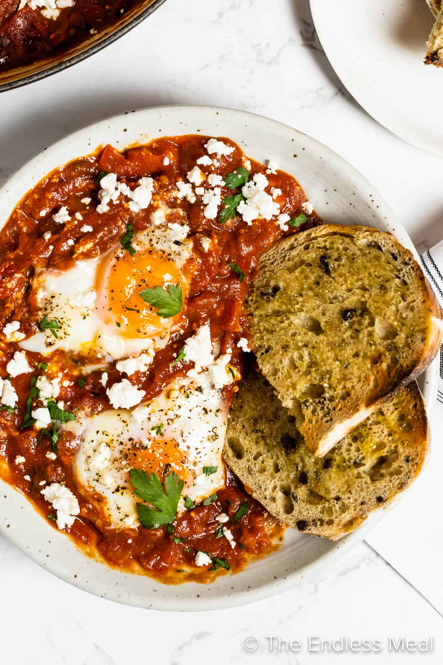 A close up of spicy shakshuka with harissa in a bowl with a slice of sourdough bread